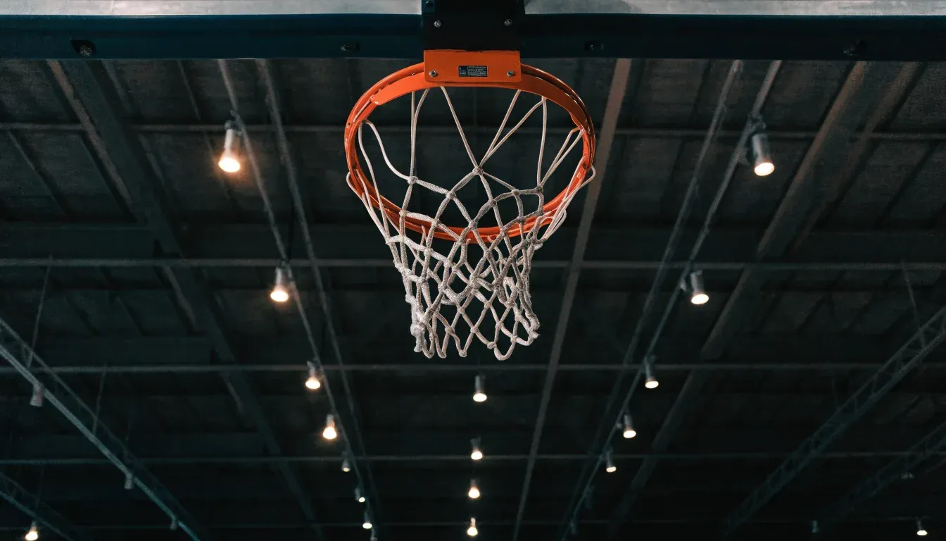 Ein Basketballkorb von unten gesehen, darüber eine Hallendecke mit Scheinwerfern und Stahlträgern.