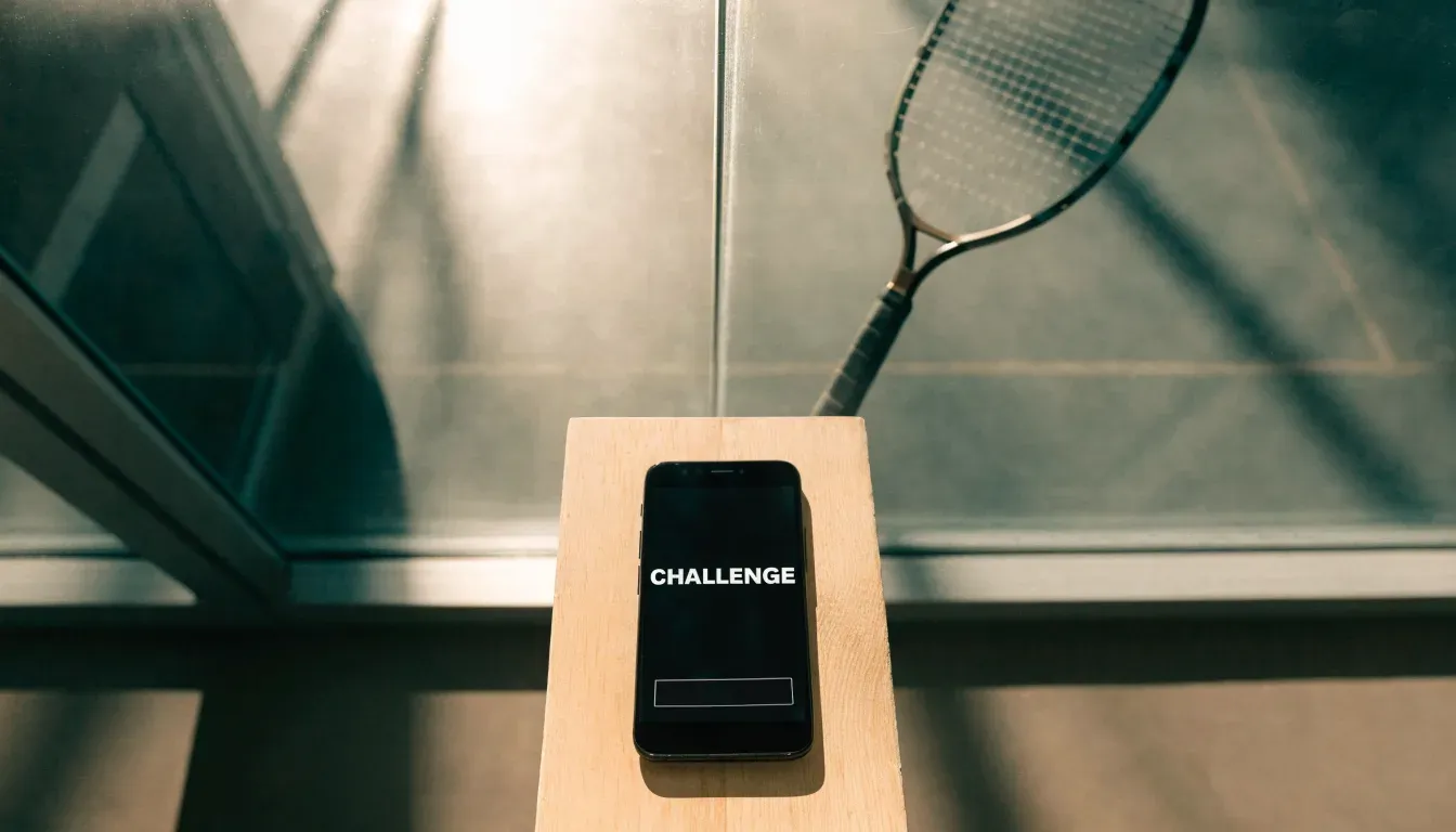 Ein Squashschläger lehnt an der Glaswand eines leeren Courts, draussen fällt Tageslicht in den Gang.