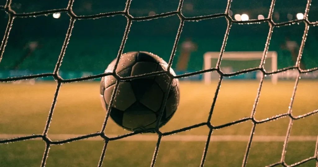 Ein Fussballnetz in Nahaufnahme, in dem ein Ball hängt, Wassertropfen glänzen auf den Maschen.